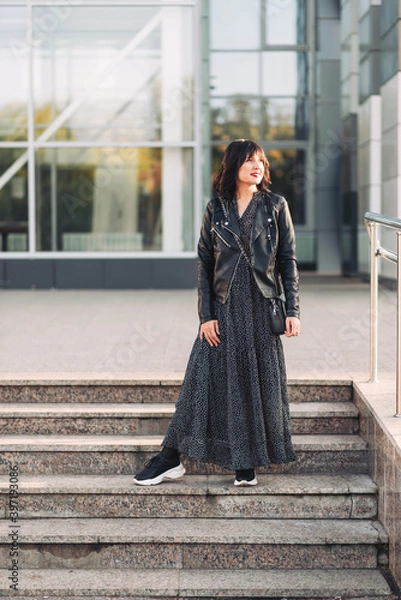Fototapeta A girl in a black jacket walks the steps in the street