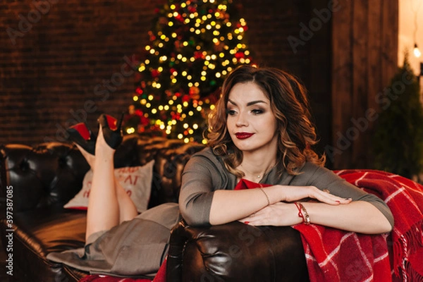 Fototapeta beautiful young girl for christmas in a happy mood against the background of a christmas tree and lights indoors