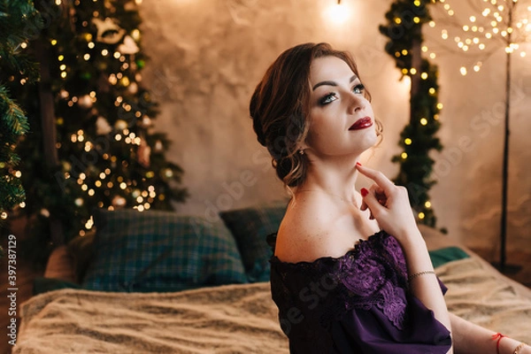 Obraz beautiful young girl for christmas in a happy mood against the background of a christmas tree and lights indoors