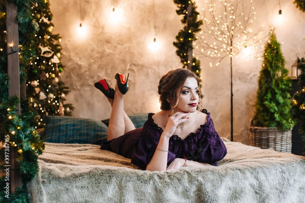 Obraz beautiful young girl for christmas in a happy mood against the background of a christmas tree and lights indoors