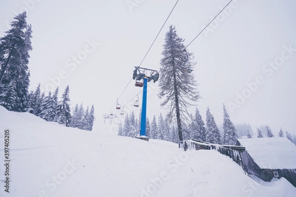 Fototapeta Ski lift with seats going over the mountain and paths from skies and snowboards.