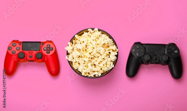 Fototapeta Two gamepads and a bowl of popcorn on pink background. Gaming, leisure and entertainment concept. Top view