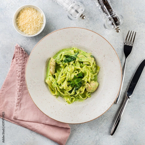 Fototapeta Pasta Tagliatelle with spinach pesto sauce and fresh basil leaves in a white platel. light background.