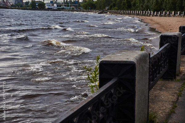 Obraz Panorama of the embankment by the lake.Along the sandy shore of the lake, there is a granite embankment, which is fenced with a cast-iron fence with pedestals. On the lake, the wind raised waves.