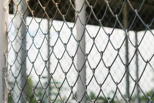 Fototapeta Selective focus Chain Link fence against blurred inside roof structure, building and sky background.