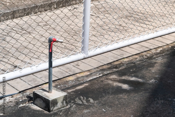 Fototapeta Water pipes with faucet on concrete ground against Chain Link fence background.