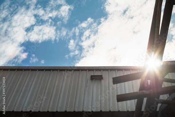 Fototapeta Low angle view edge of metal sheet roof with steel frame outside the building against blue sky and white clouds background.