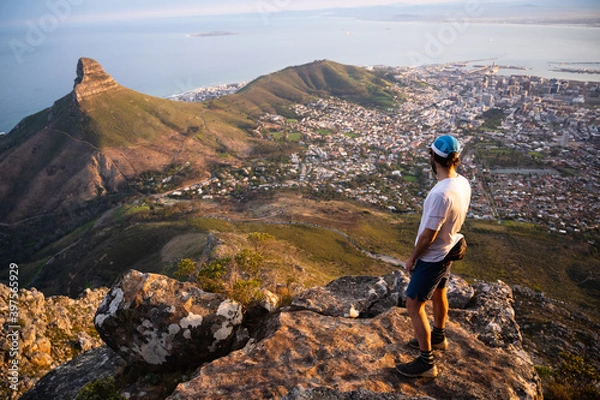 Fototapeta A fit trail runner looking down on Cape Town from the top of the mountain with a view of the city and the ocean.
