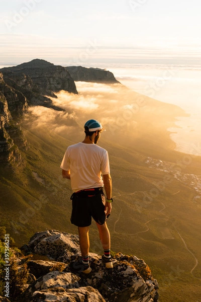 Fototapeta A trail runner enjoying the view of the sunset over the ocean from the top of Table Mountain in Cape Town