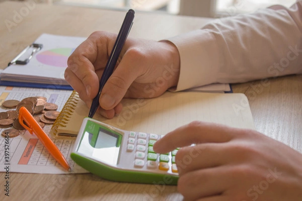 Fototapeta person writing goals on a paper, writing business plan at workplace, man holding pens, papers, notes in documents, Saving money concept, graph, stacks of coins