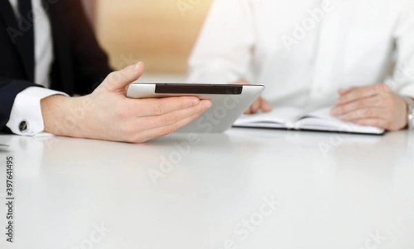 Fototapeta Unknown business people using tablet computer in sunny office. Businessman is working with his colleague at the desk, close-up