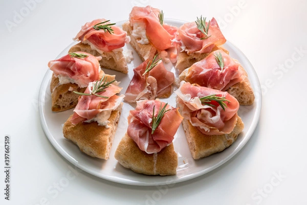 Obraz gourmet focaccia with prosciutto of Parma ham, mozzarella and rosemary sprigs, eight tasty slices of pizza on a white plate