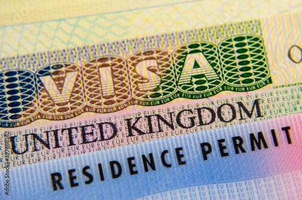 Obraz UK Biometrical Residence Permit (BRP) card placed on top of UK tourist visa sticker in a passport. Macro photo.