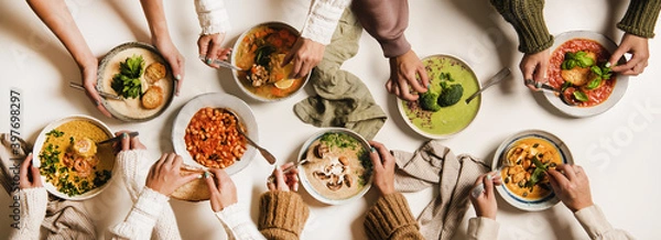 Fototapeta People eating Autumn and Winter creamy vegan soups, fall and winter vegetarian food menu. Flat-lay of peoples hands with homemade soup in plates and bread slices over white table background, top view