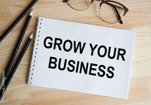 Fototapeta In the notebook the text OF GROW YOUR BUSINESS, next to pencils, glasses.