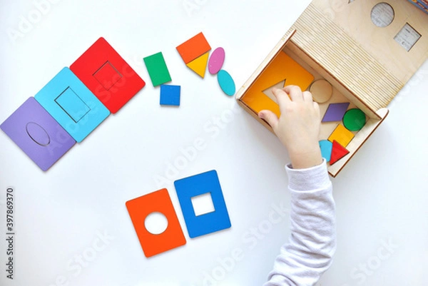 Obraz Learning colors and shapes. Children's wooden toy. The child collects a sorter. Educational logic toys for kid's. Children's hands close-up. Montessori Games for Child Development