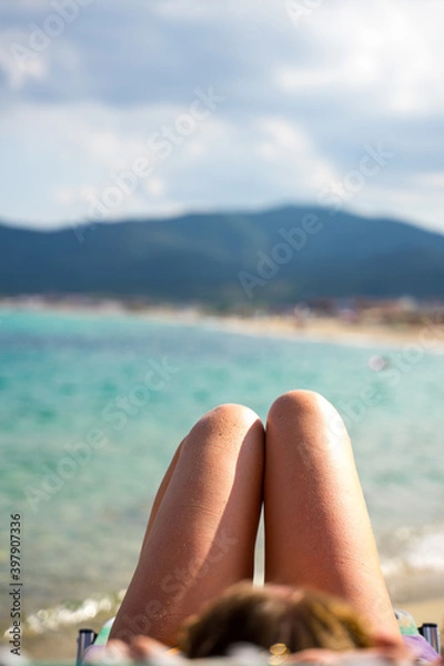 Fototapeta Girls sausage shape legs on the beach in Greece with blurred background sea 