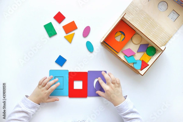 Obraz Learning colors and shapes. Children's wooden toy. The child collects a sorter. Educational logic toys for kid's. Children's hands close-up. Montessori Games for Child Development