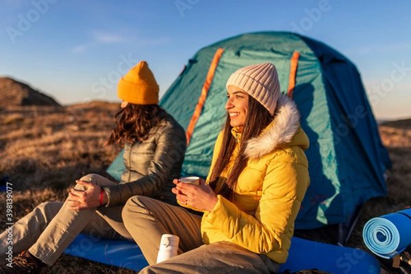 Fototapeta Two young women camping in the front of the tent at the top mountain.