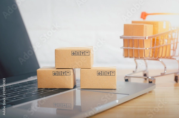 Fototapeta Brown paper boxs with laptop on wood table in office background.Easy shopping with finger tips for consumers.Online shopping and delivery service concept.