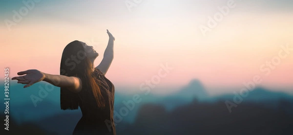 Obraz Celebration of life day concept: Happy Asian girl raised hand on blurred mountain sunrise background. Phang-nga, Thailand, Asia