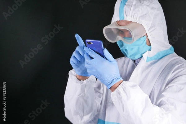Fototapeta portrait of a male doctor wearing PPE using smart phone 