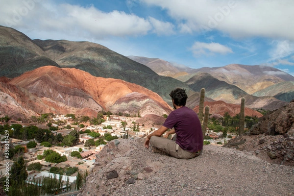 Obraz Man sitting in the mountains, looking at the town of Purmamarca.
