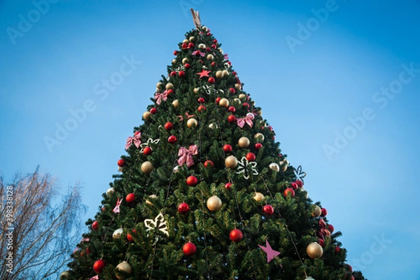 Obraz Large Christmas tree with toys on a blue sky background.