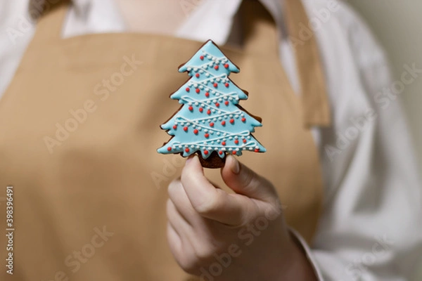 Fototapeta The pastry chef holds a gingerbread in the shape of a Christmas tree. The symbol of the new year and merry christmas.