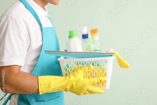 Fototapeta Young man with cleaning supplies on color background