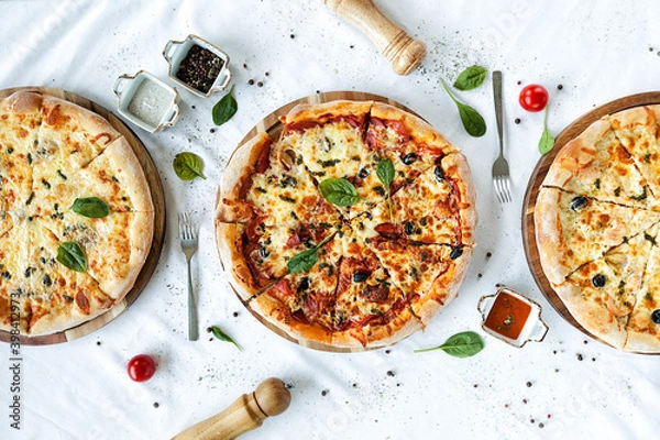 Obraz three fragrant pizzas on a white table.