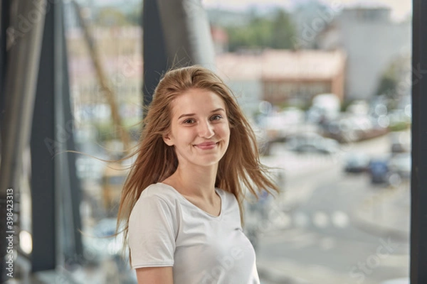 Fototapeta Happy young blonde woman with long hair flying in the wind. Against the background of iron pipes.