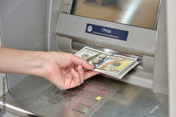 Obraz The girl's hand holds a bundle of dollar bills near the ATM.