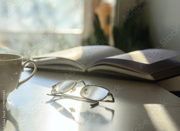 Fototapeta In front of the window on the table are glasses, a diary and a cup of coffee. Solar illumination. Concept-work at home