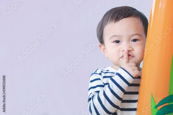 Fototapeta Asian cute baby boy doing a hush gesture, holding finger on lips, with copy free space for text.