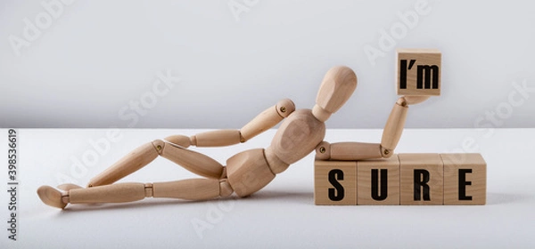 Obraz The wooden man lies near the wooden cubes with the text I'M SURE. Business concept.