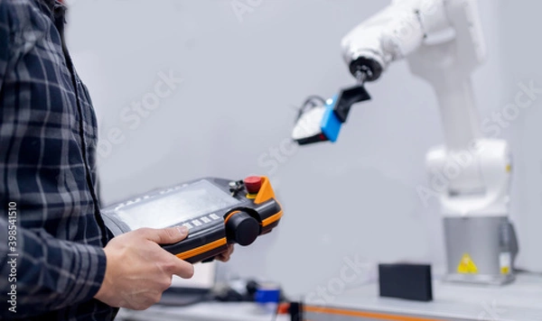Fototapeta Engineer operator controls automatic mechanical arm robot to weld