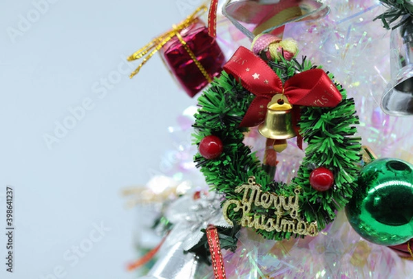 Fototapeta Focus and soft lens Christmas tree decorated with colored balls and gift boxes with Christmas wreath and silver bells on white background.