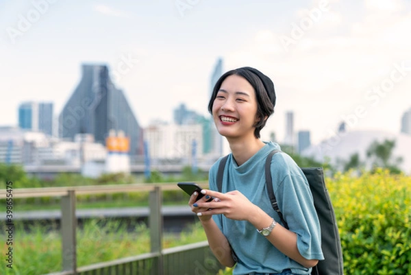Obraz 5G smart communication technology makes people comfortable. Cheerful girl using a cellular mobile phone on a sidewalk. Woman having fun with smartphones in garden park. Living in the capital city