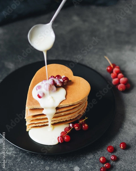 Obraz Breakfast for lovers. Pancakes in the form of a heart. Pour sweet cream on top with a spoon and garnish with fresh red currant berries. Ideas for Valentine's Day. American pancakes are stacked.