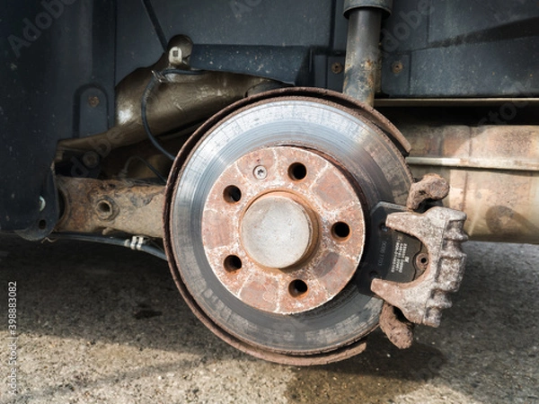 Fototapeta Brake disc system, pads and shield of vehicle without wheels for repair or replacement close up, suspension of car, process of new tire replacement, service concept, maintain rusty car parts