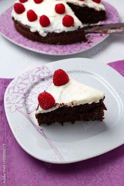 Fototapeta Delicious chocolate cake with cheese cream on top and raspberries. Christmas cake. Selective focus. Copy space.