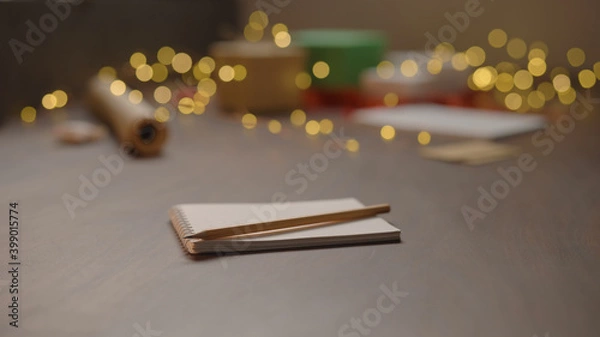 Fototapeta Notepad with pencil on walnut wood table with christmas lights on background