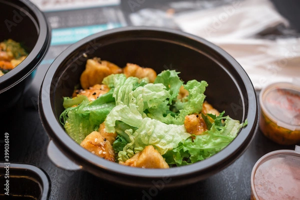 Fototapeta Salad with chicken, fresh salad and sesame seeds in a plastic plate on a black table