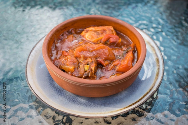 Fototapeta Georgian chicken dish with vegetables and spices in a beautiful craft plate on a glass table