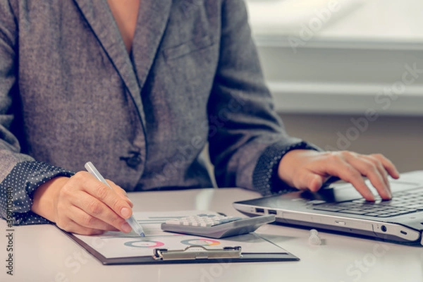Fototapeta Close up of woman`s hands working with financial data using calculator
