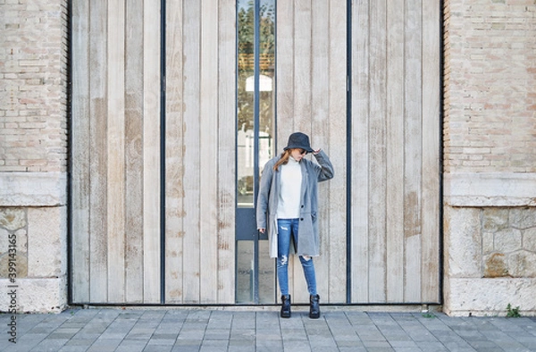 Fototapeta Portrait young pretty Caucasian girl with sunglasses, dressed in a gray jacket and a white sweater and a hat.