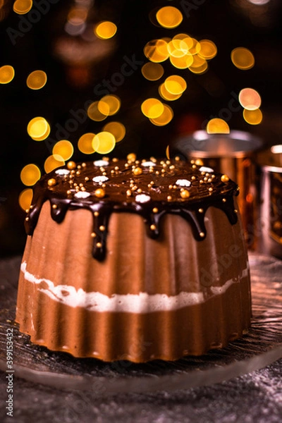 Fototapeta Tasty Three Chocolates mousse cake with ganache in Christmas and New Year decorations. Chocolate cake with layers. Bokeh lights background. Vertical orientation. Christmas Eve. Low Key.