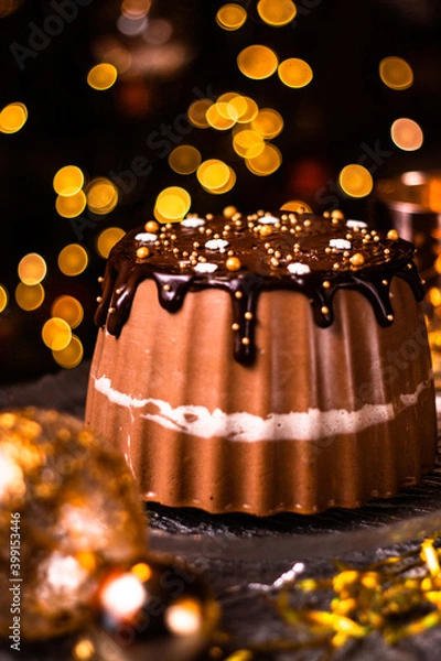 Fototapeta Tasty Three Chocolates mousse cake with ganache in Christmas and New Year decorations. Chocolate cake with layers. Bokeh lights background. Vertical orientation. Christmas Eve. Low Key.