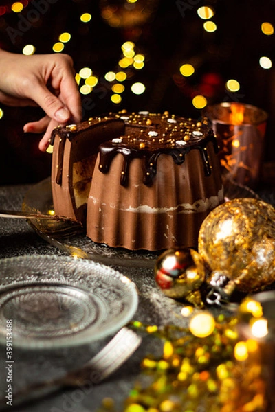 Fototapeta Cutting tasty Three Chocolates mousse cake with ganache in Christmas and New Year decorations. Chocolate cake with layers. Bokeh lights background. Vertical orientation. Christmas Eve. Low Key.